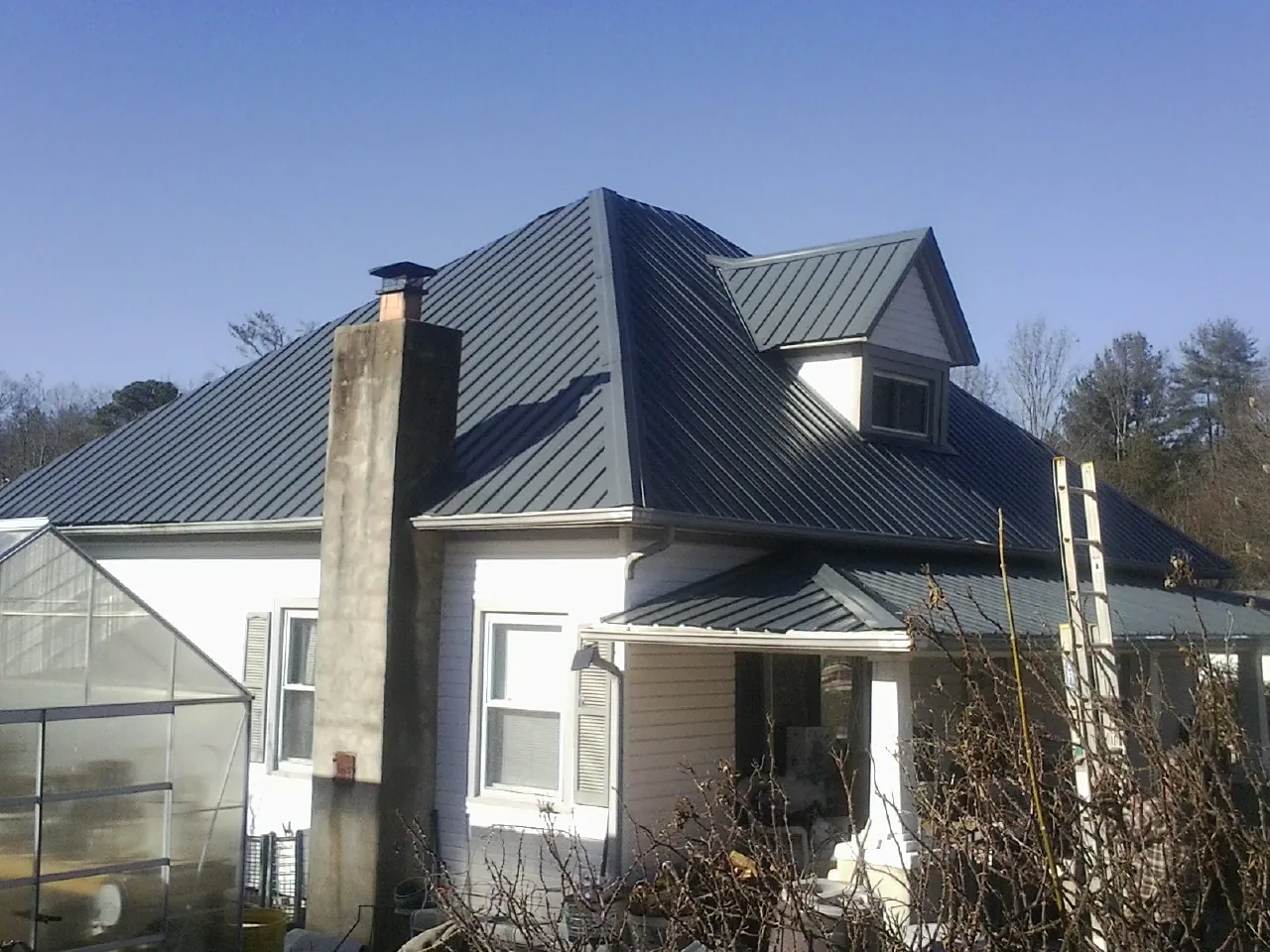 Dark blue standing seam metal roof on a white farmhouse with dormer — Slate & Tile Roof Repair by Roofing Brothers in Locust Dale
