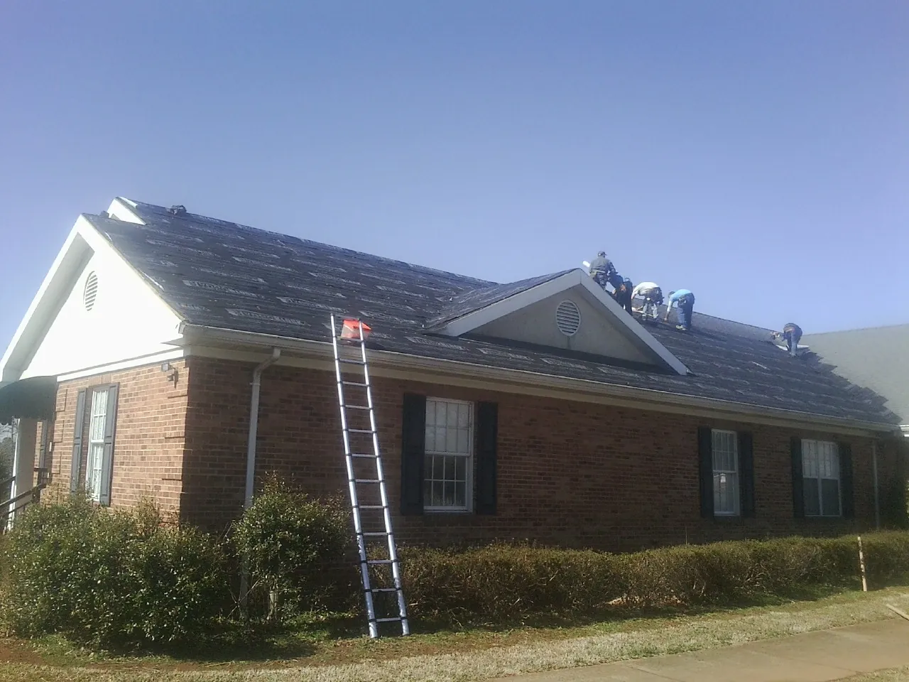 Crew tearing shingles off a brick ranch roof with a ladder set — Metal Roof Repair work by our crew in Locust Dale