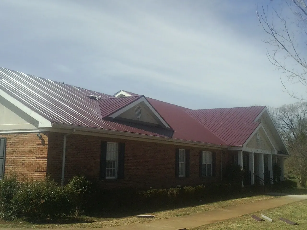 Red metal roof with gabled entries on a long brick building, from a Hail Damage Roof Repair job in Locust Dale