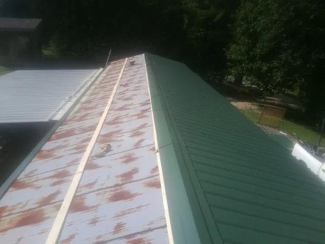 Old rusted panels beside newly installed green metal roofing — Wind Damage Roof Repair by Roofing Brothers in Locust Dale