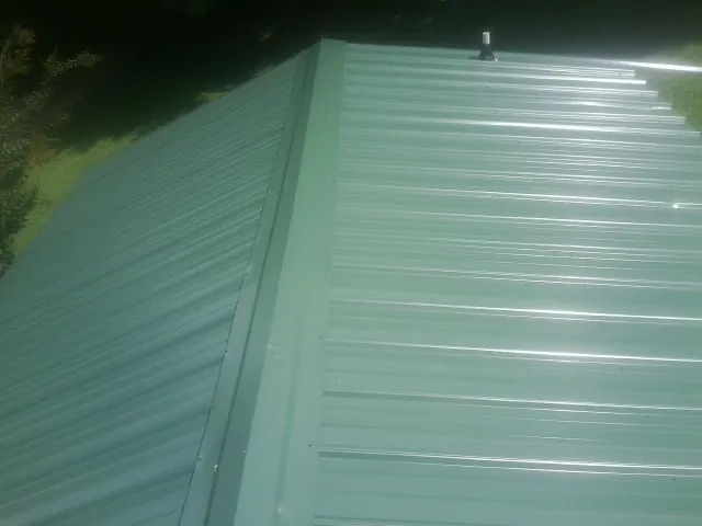 New green metal panels meeting at the ridge of a roof — Flat Roof Repair work by our crew in Locust Dale