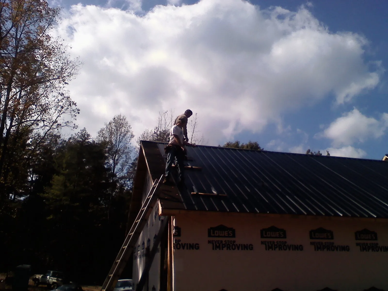 Roofer fastening dark metal panels high against a cloudy sky, from a Roof Inspection job in Locust Dale
