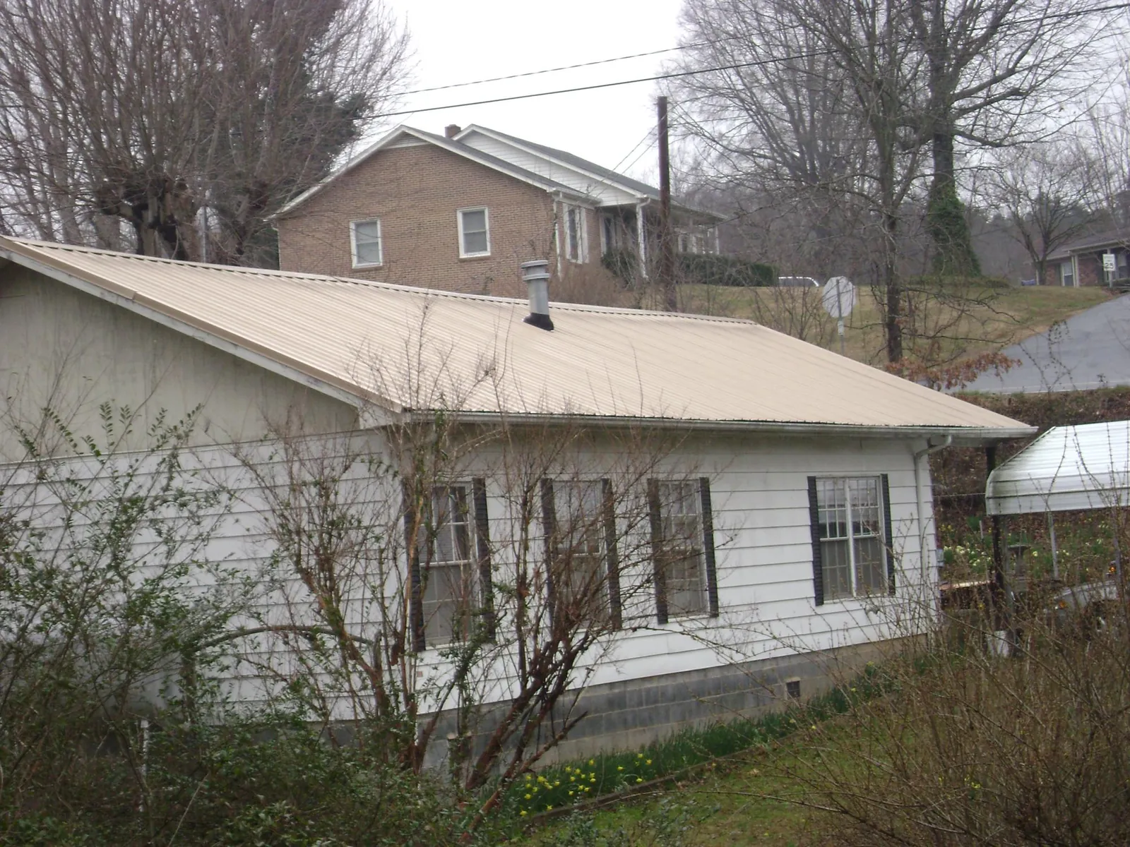 Tan metal roof on a white sided house set into a hillside — Commercial Roofing by Roofing Brothers in Locust Dale