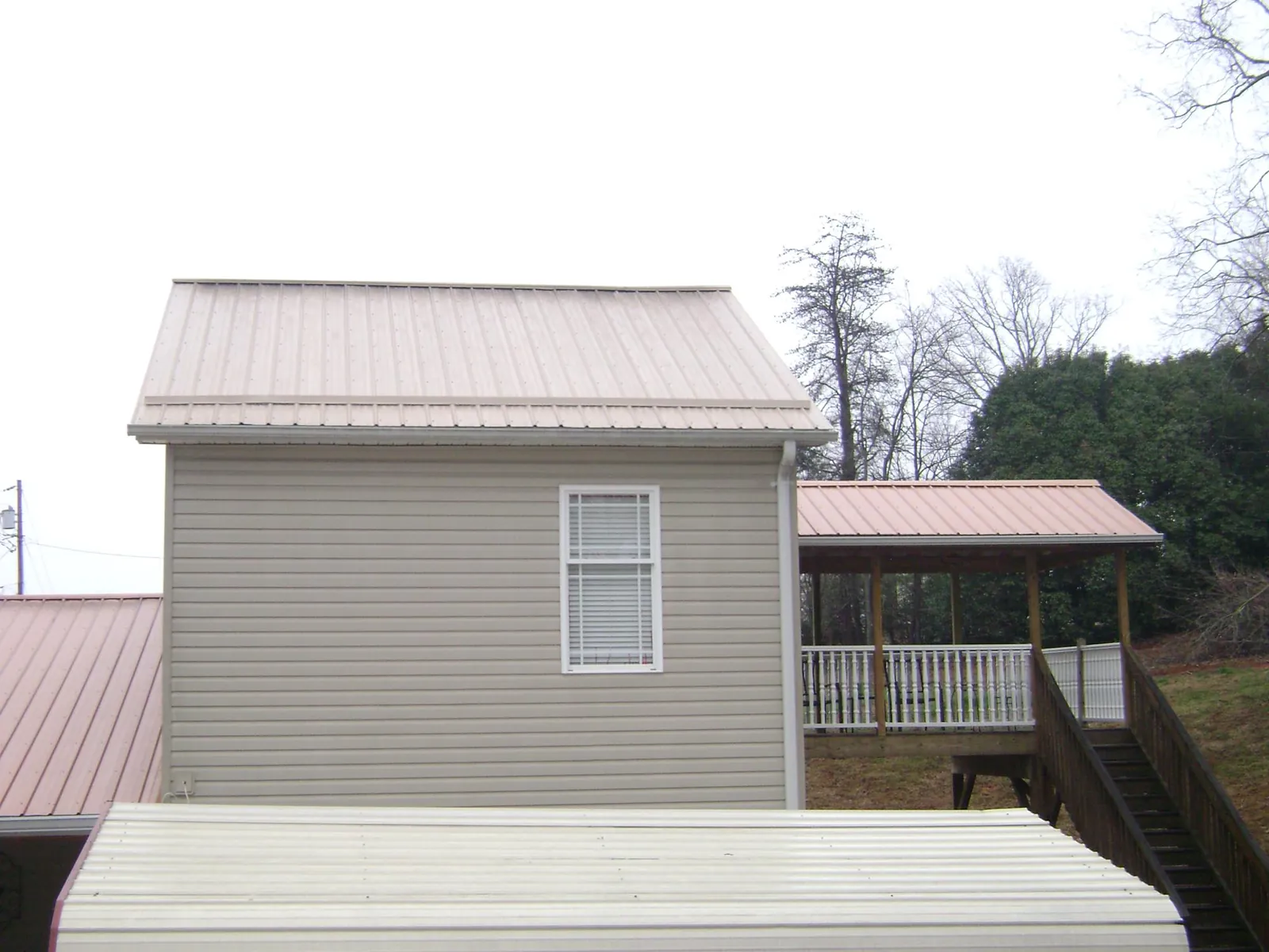 Tan metal roofs on a two story addition and attached porch, from a Roof Replacement job in Locust Dale